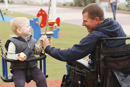 Disabled Father play with his little son on the playground.