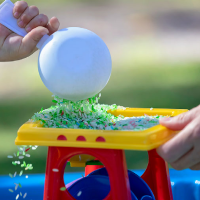 Child is pouring rice out of a scoop into a messy play toy